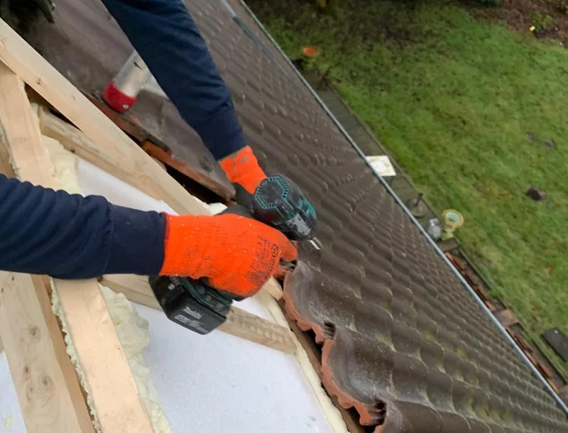 Werk aan de houten latten tussen de dakpannen, met een accuschroefmachine.
