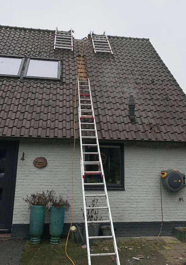 Een woning met een ladder langs de gevel en een schoorsteen boven het pannendak.
