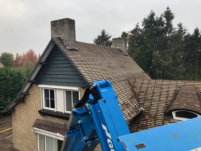 Twee schoorstenen op een pannendak, met een hoogwerker naast de woning.