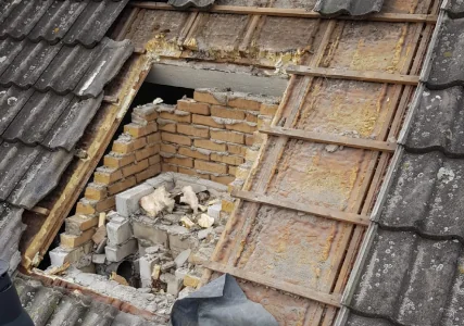 Dakpannen en daklatten zijn plaatselijk weggenomen; er ligt los metselwerk in de opening.