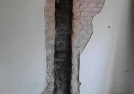 Een geopend kanaal in een gepleisterde wand, met donkere aanslag op het metselwerk.