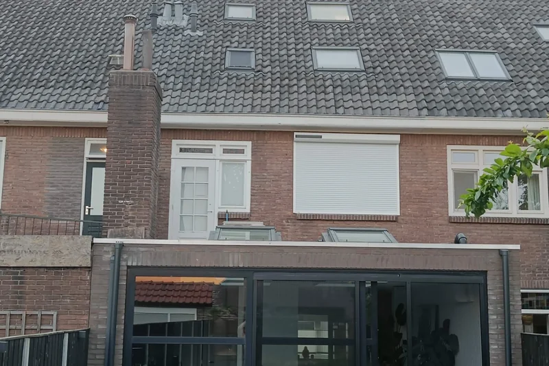 Een gemetselde schoorsteen loopt langs de achtergevel omhoog tot boven het pannendak.