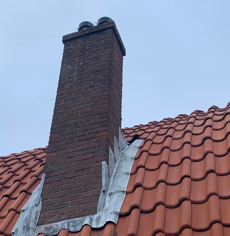 Gemetselde schoorsteen met loodslabben op een rood pannendak.