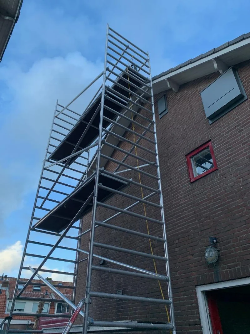 Een steiger langs een gemetselde kopgevel, tot boven de dakrand.